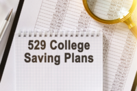 Spreadsheet in background with numbers on it and a magnifying glass in the upper right corner and a steno notebook with 529 College Savings Plans written on the top sheet