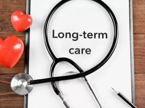 Long-Term Care written on a piece of paper on a desk with a stethoscope wrapped around it.